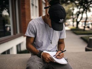 Man writing with left hand in a notebook on his lap