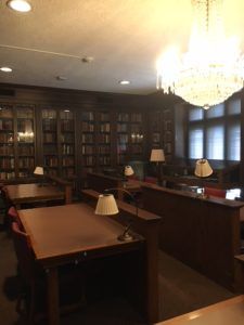 Dark wood bookshelves line the walls of a room with reading tables and a large crystal chandelier