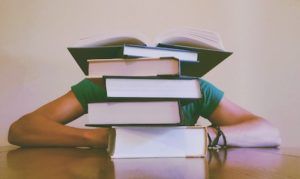 Person crouches behind a pile of books.