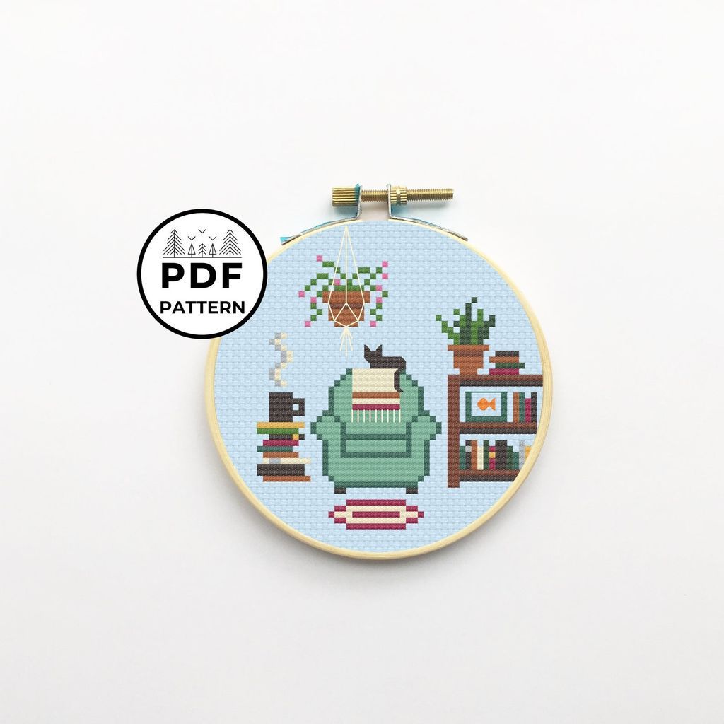 Cross stitch of a reading chair, bookshelf, plants, and steaming hot beverage