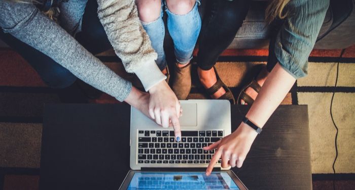 a photo of several hands pointing at a laptop screen