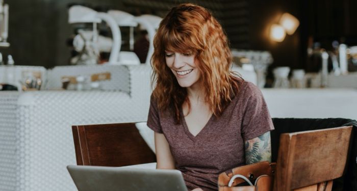 woman sitting on brown chair looking at silver laptop