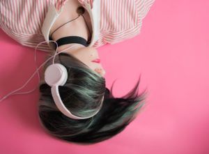 a person with black and grey hair swept over their face seen upside down wearing over-ear headphones against a pink background