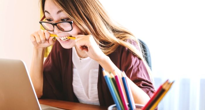 woman biting pencil while sitting on chair in front of computer during daytime