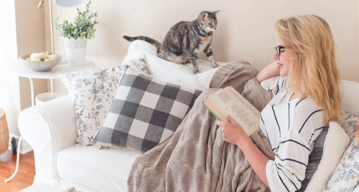 a photo of a woman under a blanket reading with a cat by her side