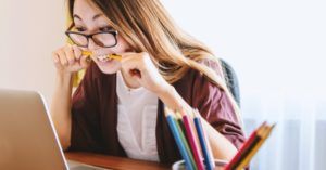 a stressed student biting a pencil while staring at a laptop computer screen