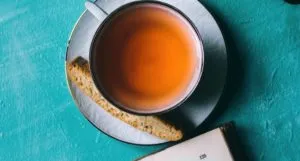 cup of tea with scone on serving plate against teal background with the corner of a book peeking at the bottom