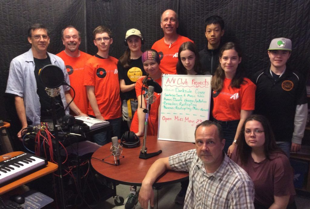 Group of students and adults standing near mic and poster that says, "A/V Club Projects"