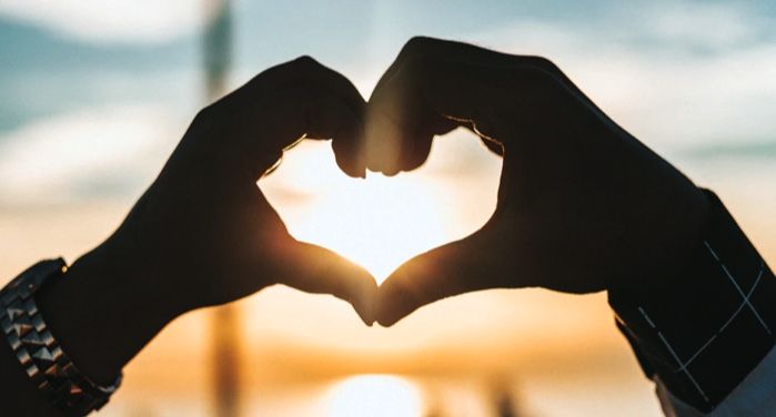 two hands joining to make the shape of a heart with sun setting in the background