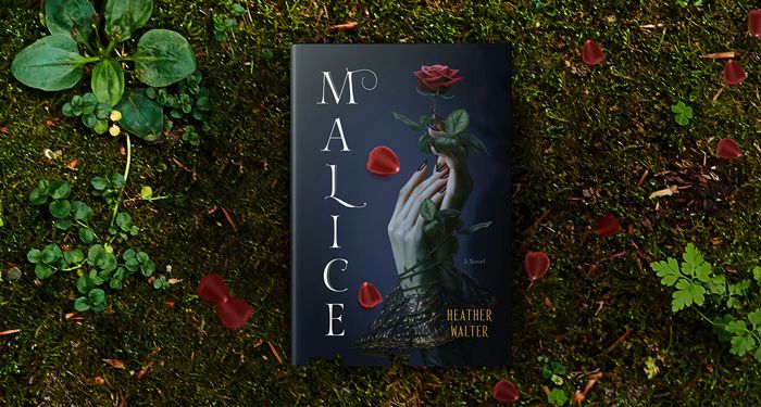 a copy of MALICE by Heather Walter against a backdrop of dirt and green plants with red flowers