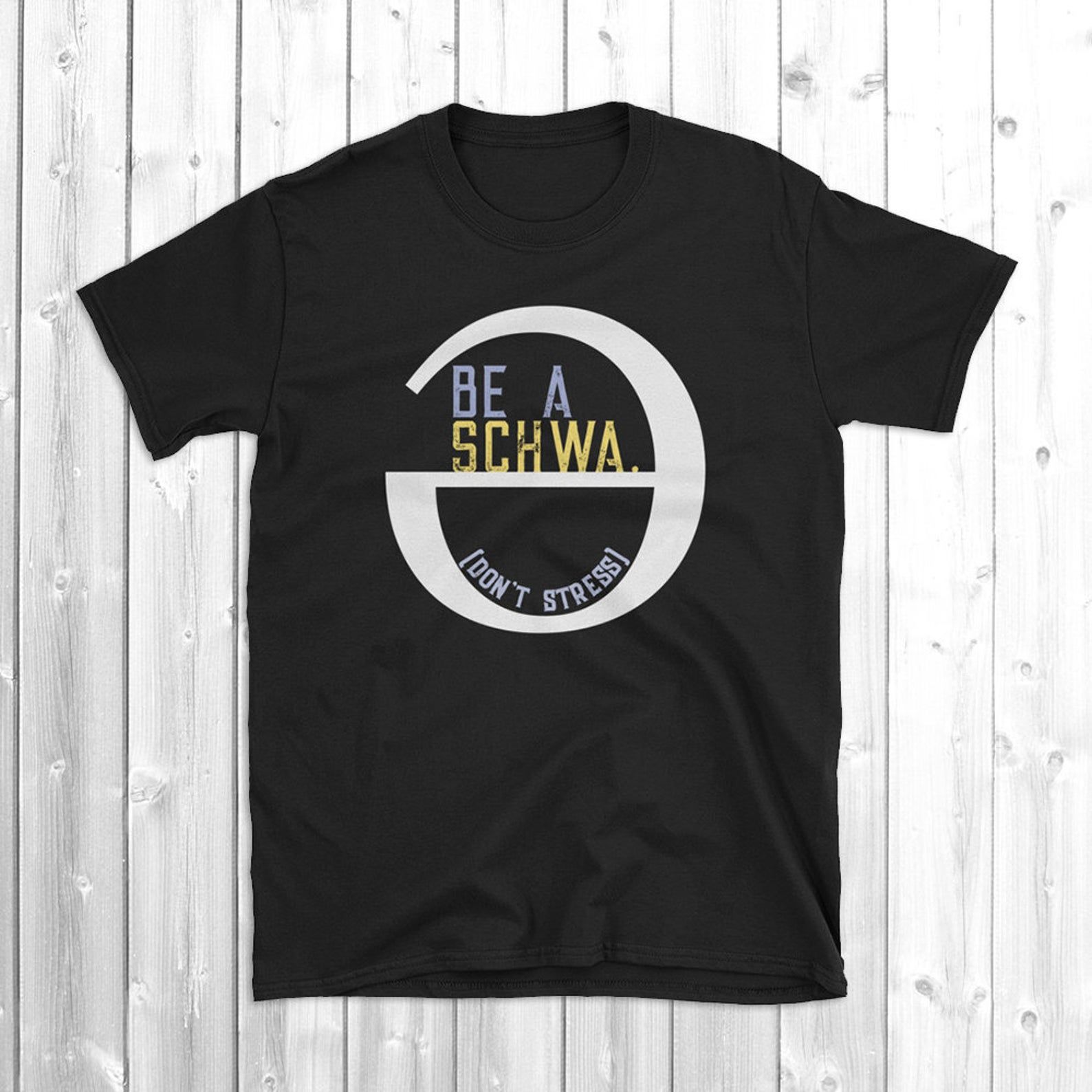 Black t-shirt with a big white 'schwa' sign on it (an upside-down and backwards e.) The text inside the schwa reads: "Be a Schwa. [Don't Stress]"