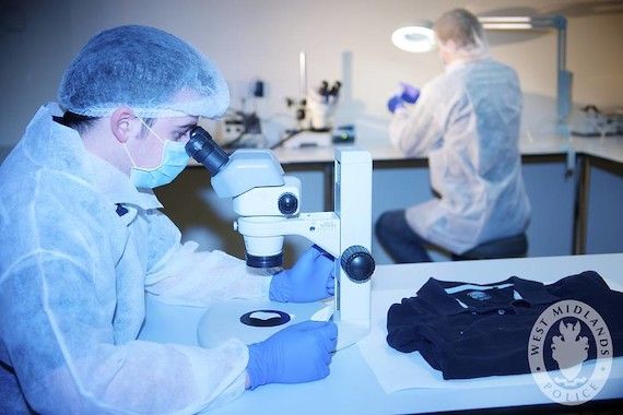 Person in scrubs and protective gear looks through microscope