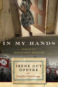 Book cover for In My Hands, showing a woman in a floral dress walking through a door above the title. Beneath the title, nazi flags are visible on a sepia toned street.