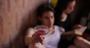 A person holding a drink while an out of focus figure behind them reads
