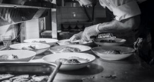 chef bends over to garnish dishes in black and white picture