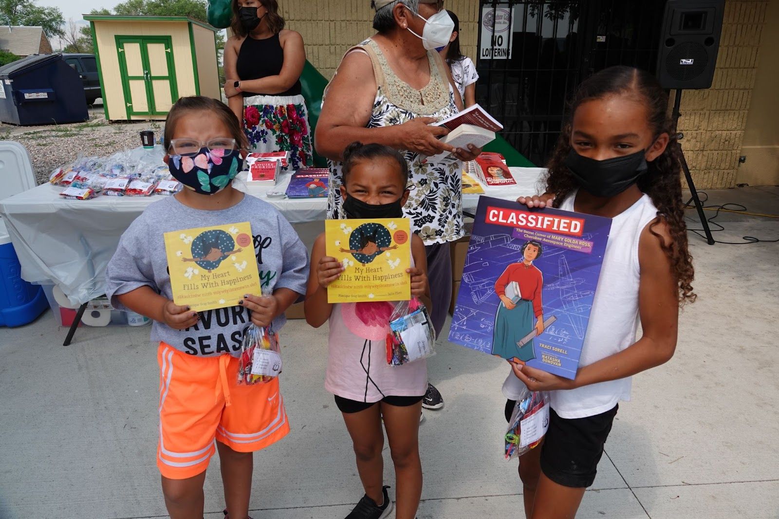 Three children hold books from the Little Free Library opening ceremony. Image provided by Little Free Library.