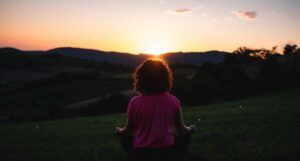 woman sitting cross-legged on grass at sunset https://unsplash.com/photos/WP77TQnwTr4