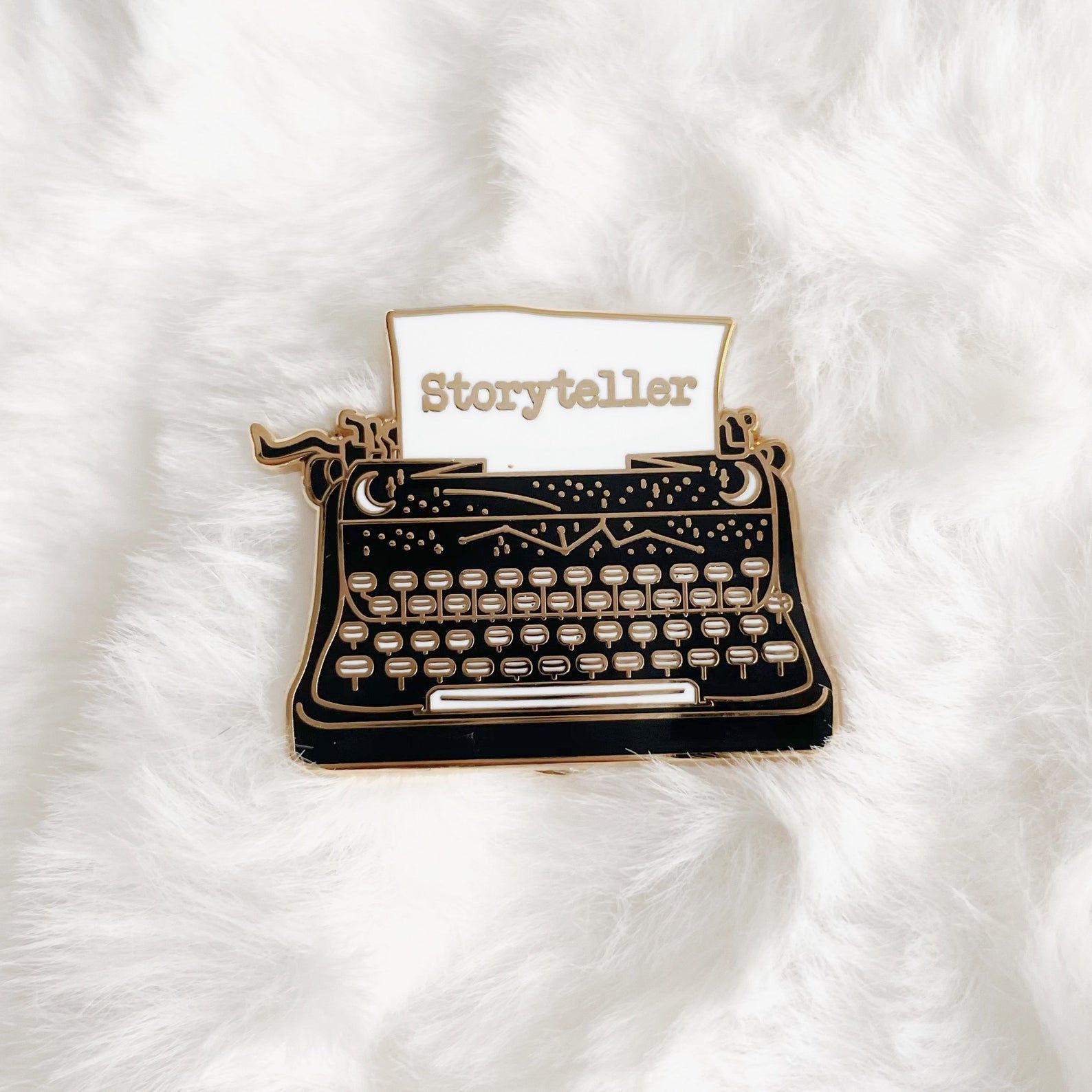 Image of black typewriter pin with white paper. text on paper reads "storyteller."