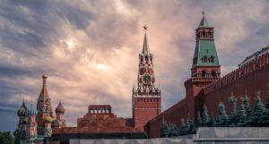 A landscape of Moscow under a bright cloudy sky, showing the towers of St Basil's Cathedral and the high red walls of the Kremlin