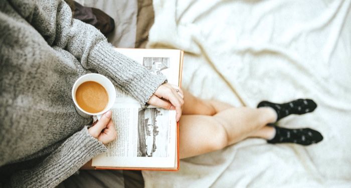 person holding a coffee cup and n open book on their lap