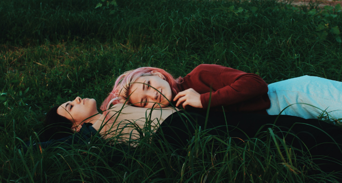 a woman lying in a field with another woman laying her head on her stomach