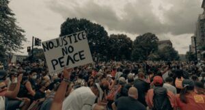 image of a large protest. Someone is holding a sign that reads No Justice, No Peace