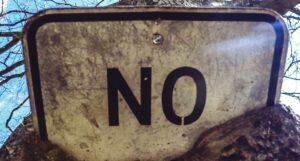 a black and white no smoking sign; sign is partially buried in dirt, so only word visible is "no"