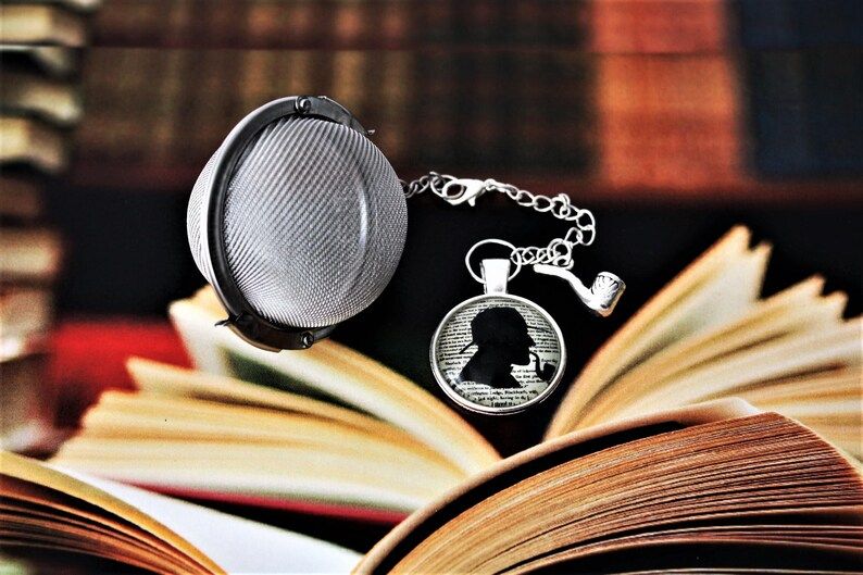 ball style tea infuser with a smoking pipe charm and a cabochon with sherlock's silhouette in his iconic deerstalker hat and a pipe in his mouth