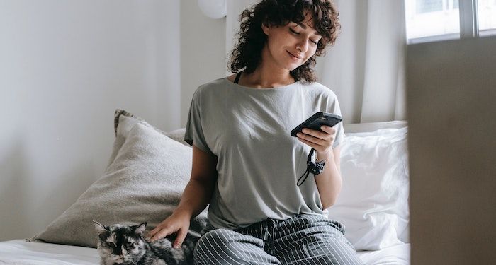 woman smiling at phone and petting cat