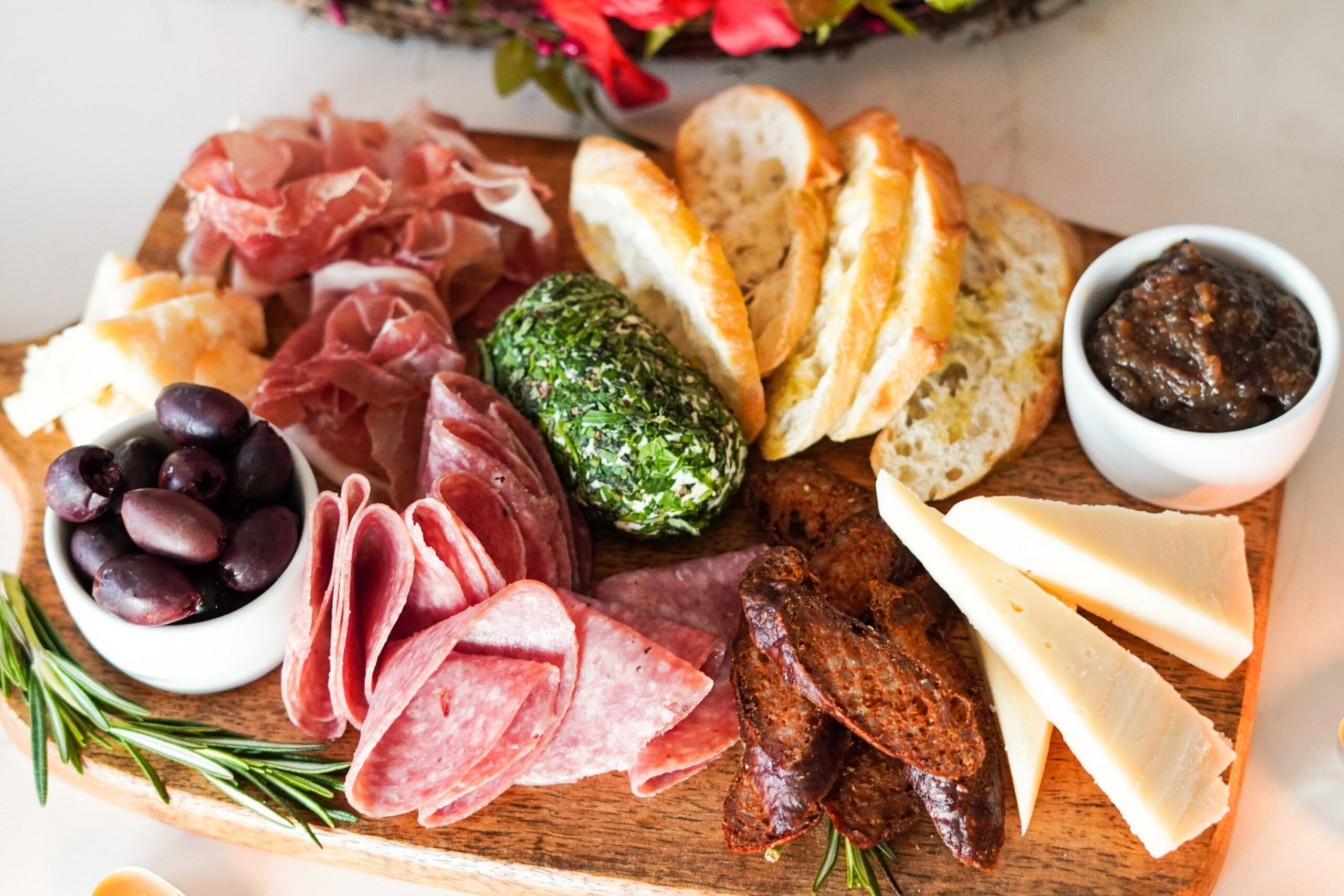 cutting board with olives, deli meat, cheese wedges, and sliced bread