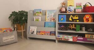 a kids reading nook including a plant, two kids size bookshelves, and a basket of books