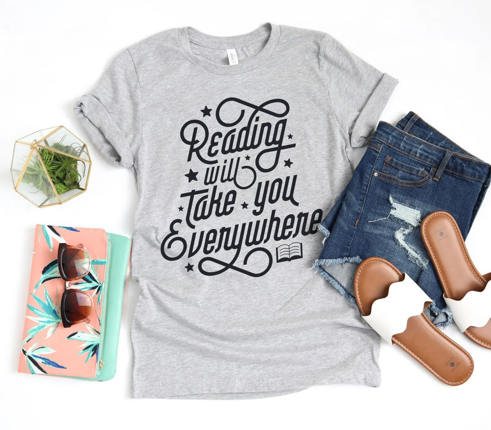 Image of a grey t-shirt with the words "reading will take you everywhere" in vintage, scripty font.
