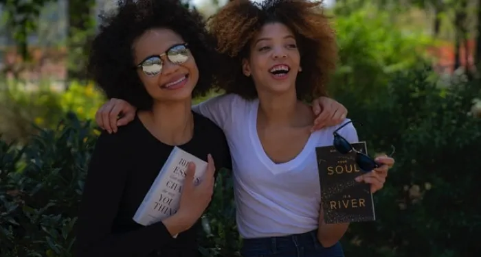 two women smiling, hugging, and holding books