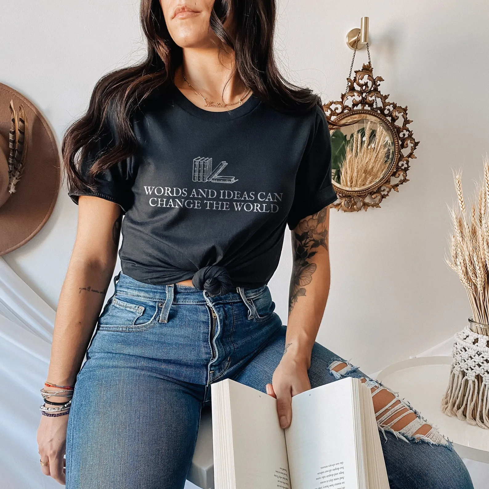 Image of a woman wearing a shirt that reads "words and ideas can change the world." The shirt is black with books on it.