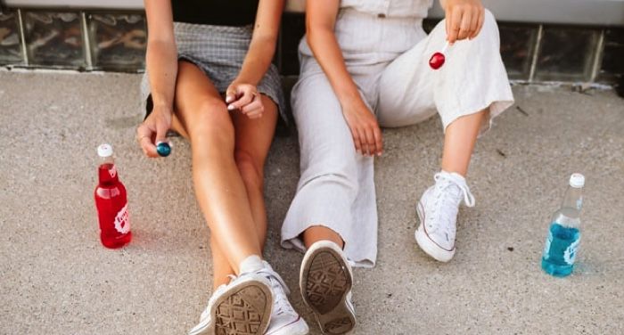 two people sitting on the sidewalk with sodas