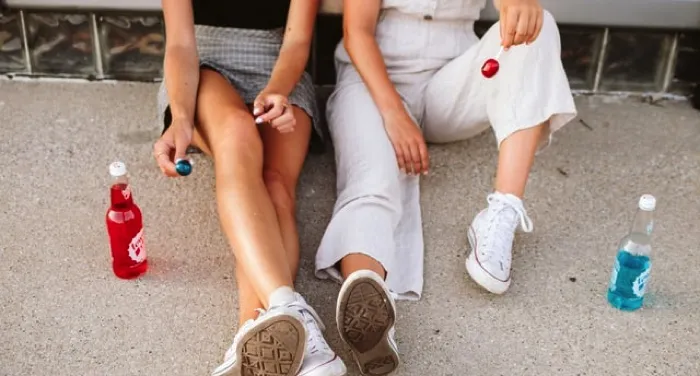 two people sitting on the sidewalk with sodas