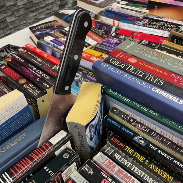 A box of true crime books with a prop knife wedged in them