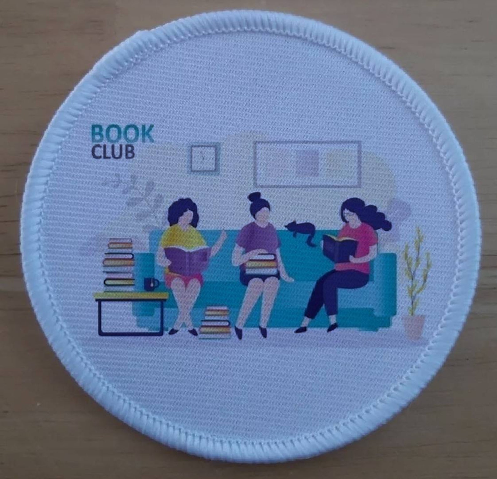 sew-on patch showing three women reading on a sofa, with a cat, and the words Book Club on the wall. 