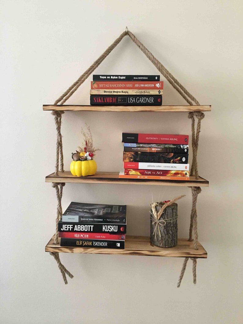 three tiered shelves held together by rope hanging from a wall, with books on every shelf
