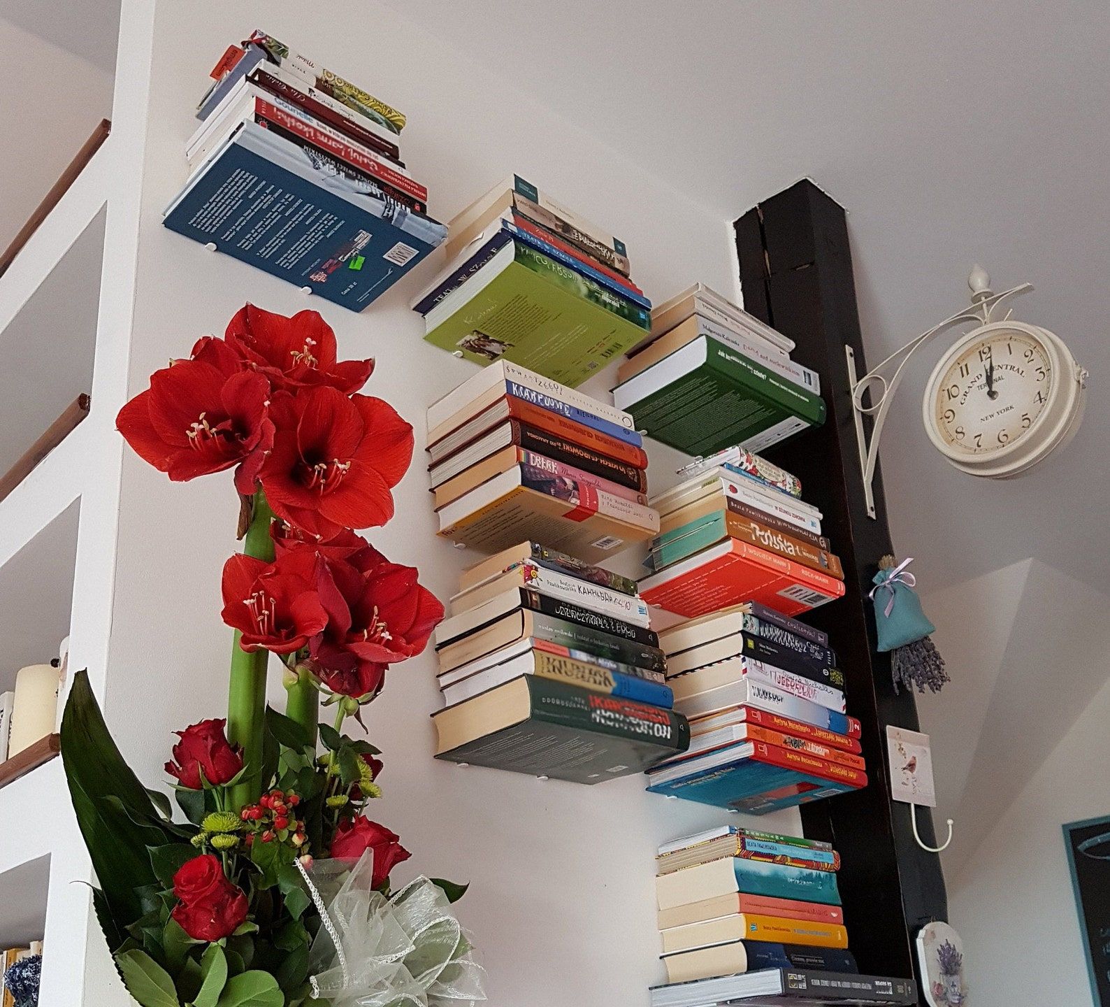 invisible floating metal bookshelves piled with books along a wall, next to a flowering plant