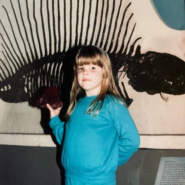 a photo of young Isabelle Popp, posing in front of a Dimetrodon fossil
