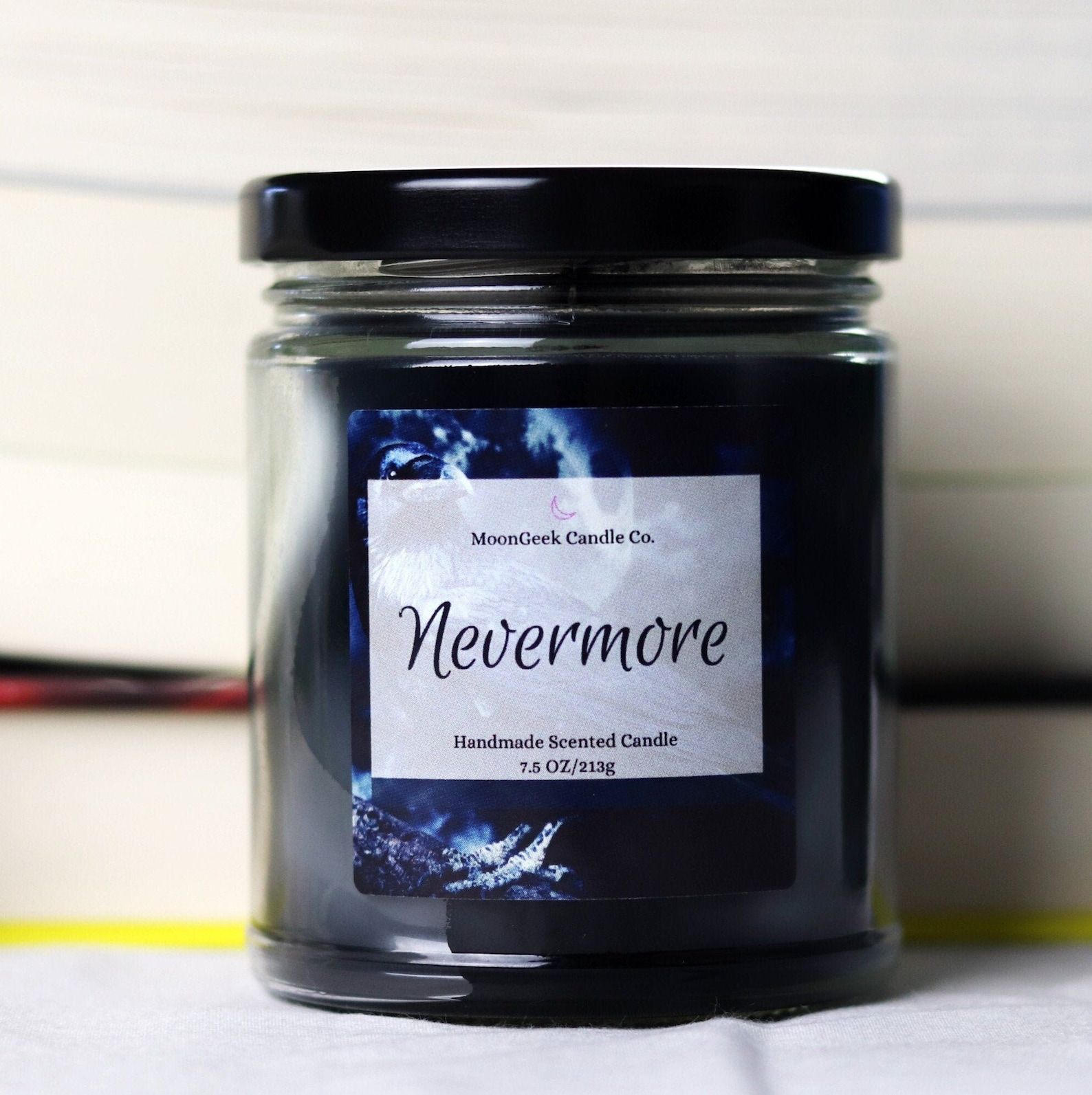 A dark blue candle in a glass jar with a white label that reads "Nevermore"