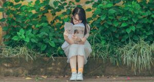 a woman reading a book in front of a wall of plants