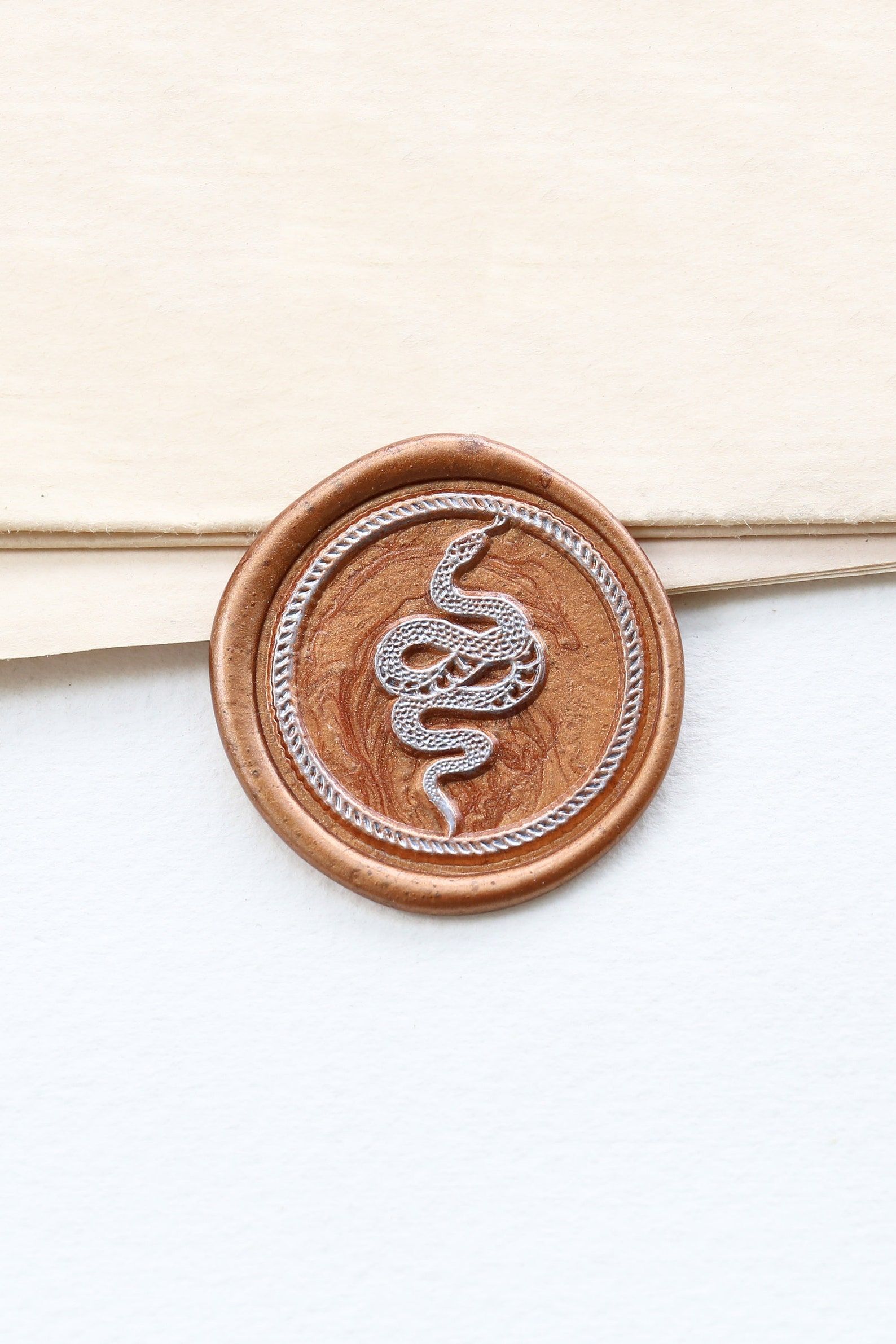 Image of a gold wax seal with a snake in the center. 