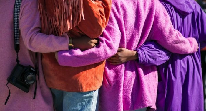 four women in purple holding each other with backs to the camera