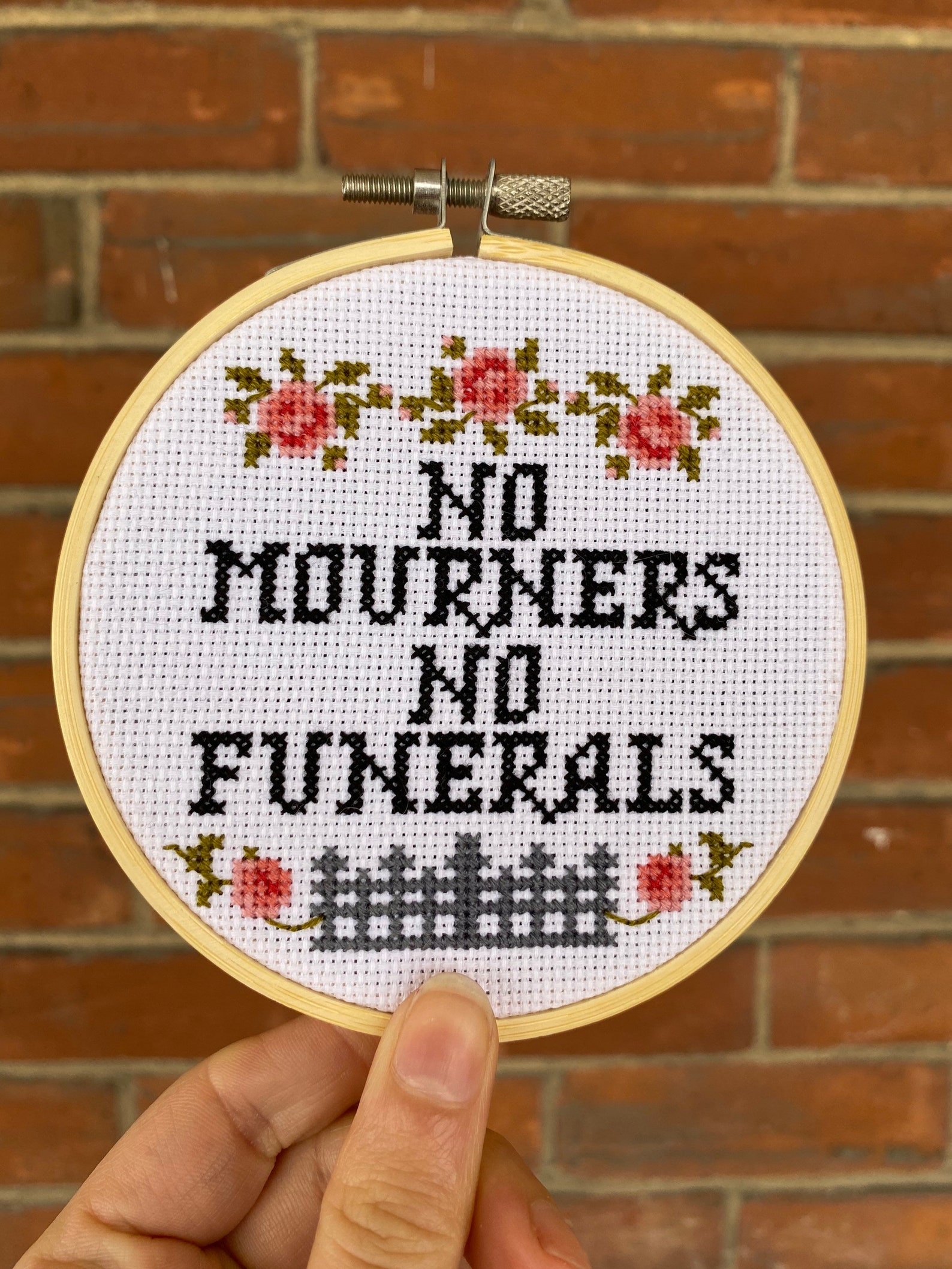 Circular hoop cross stitch with "no mourners no funerals" at the center and decorated with roses
