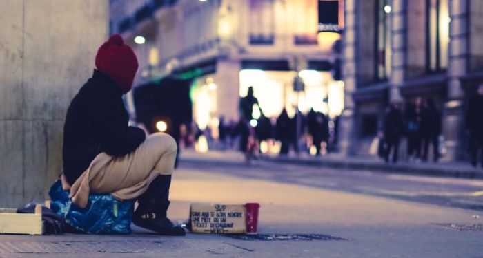 person sitting on sidewalk with a sign and a cup