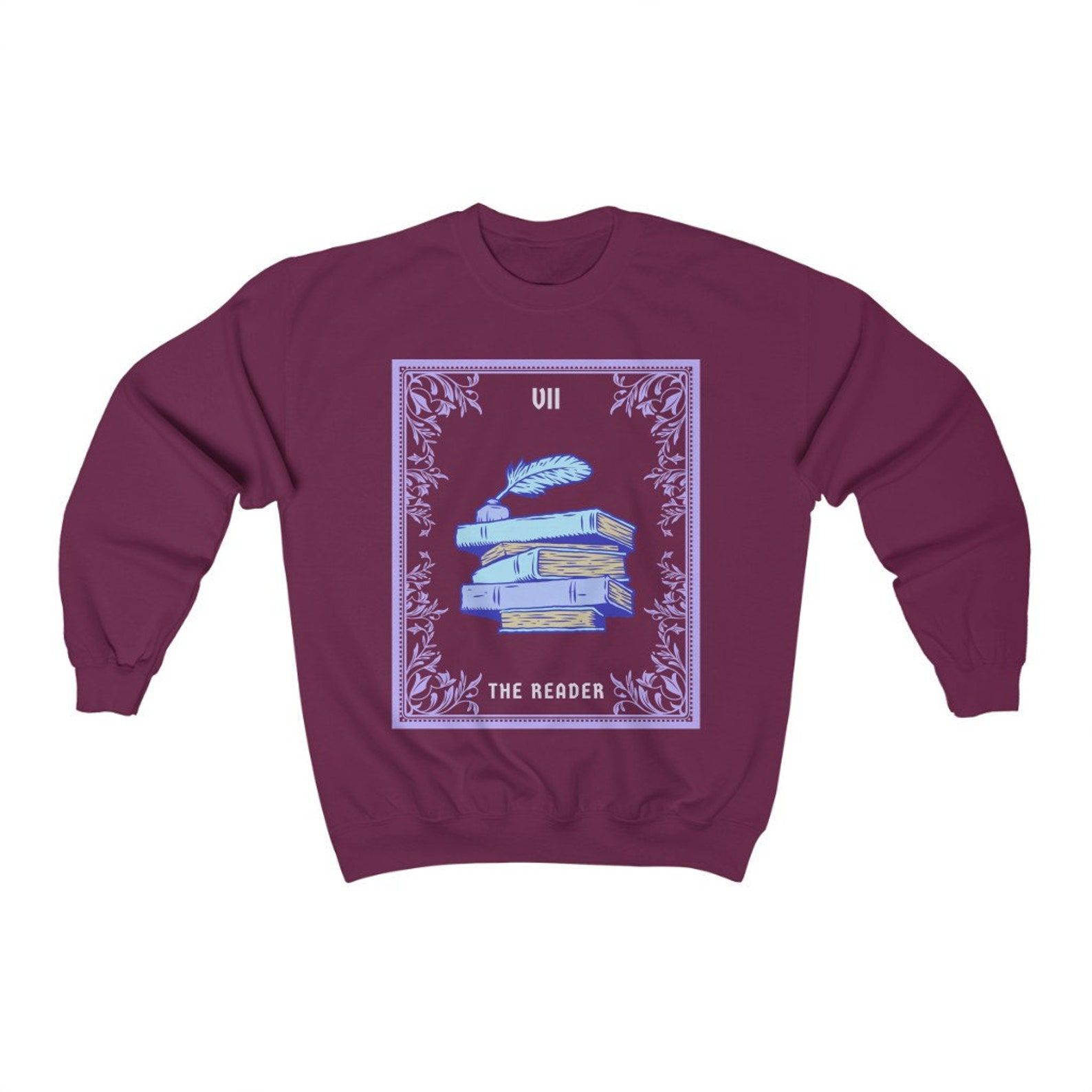 Purple sweatshirt with a tarot card design in the center. It's "The Reader" and featured a stack of purple and blue old books, along with a feather pen. 