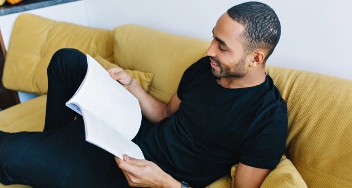 Image of a Black man reading on a yellow couch