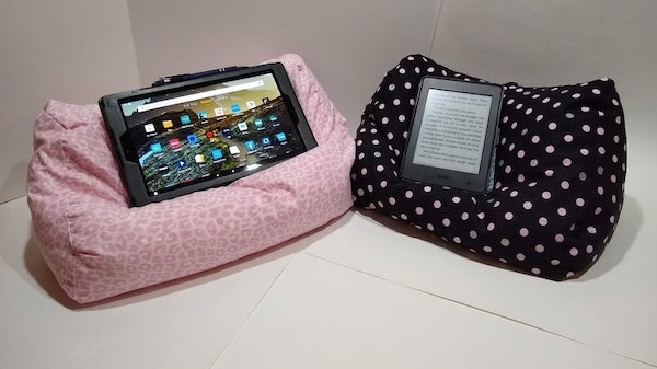 Two reading pillows (one pink cheetah print and one black with white polka dots) each holding a tablet/e-reader